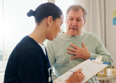 man holding his chest describes pain symptoms to nurse with clipboard